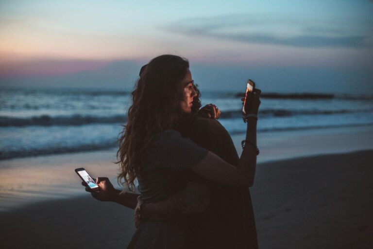 a photo of a couple hugging while using smartphones reflecting that social media isn’t couples therapy