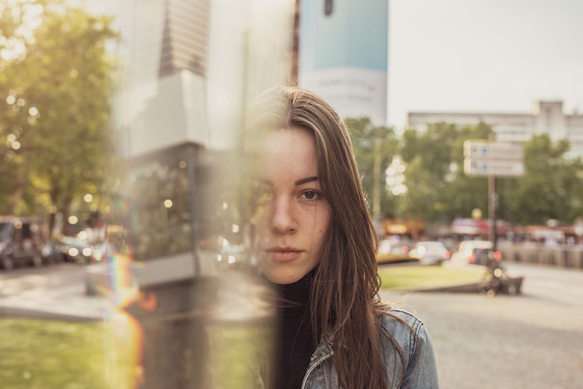A woman gazing through a glass window, reflecting on the cityscape, representing the illusion of the self.