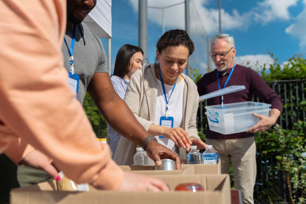 A group of people gathers around a food donation box, participating in a charitable giving event.